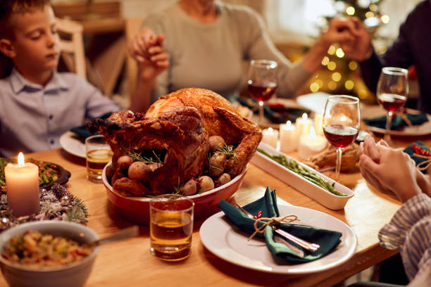 istock Thanksgiving turkey with family saying grace at dining table. 1349700521