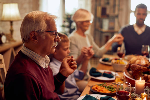 istock Senior man and his family saying grace while having Thanksgiving dinner at dining table. 1349700627