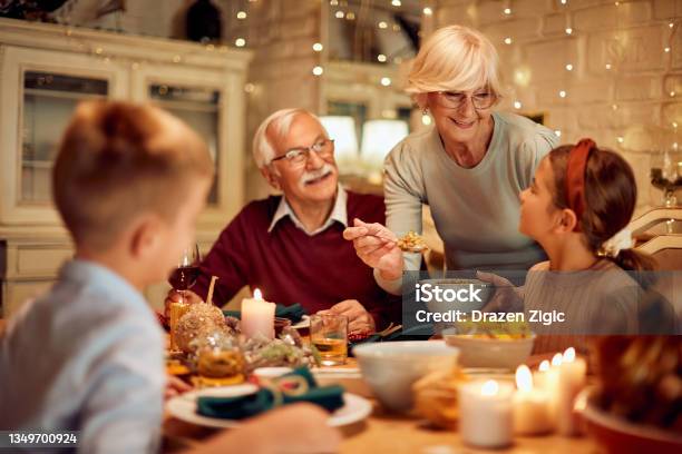 Happy Senior Woman Serving Food To Her Family During Thanksgiving Meal At Dining Table Stock Photo - Download Image Now