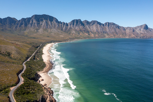 Aerial image flying over waves breaking against the beautiful South African coastline near Cape Town. Aerial view over a coastal road near False Bay in Cape Town, South Africa
