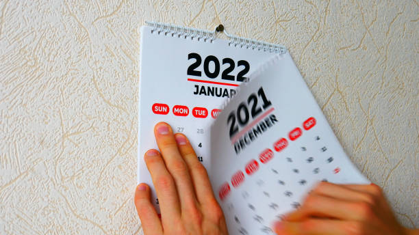 nahaufnahme der hände eines mannes, der die dezemberseite eines kalenders 2021 an der wand abreißt, gefolgt von der januar-seite eines neuen kalenders 2022 - kalender abreißen stock-fotos und bilder