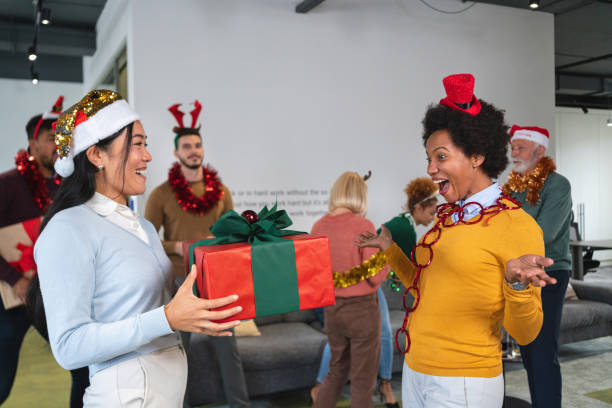 compañeras de trabajo de grabado asiático y afroamericano intercambiando regalos de navidad durante la fiesta de oficina - businessman 30s low key surprise fotografías e imágenes de stock