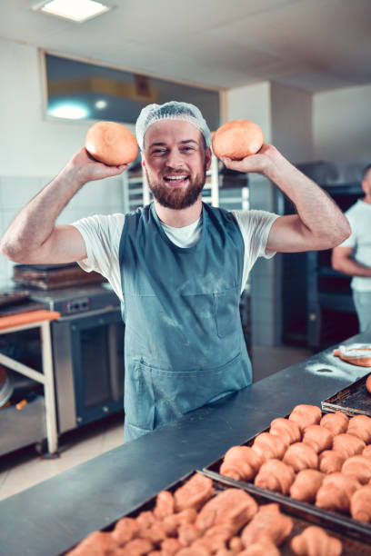 istock Smiling Baker Showing Two Bread Buns Freshly Baked In Bakery 1349704797