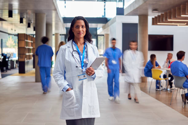 Portrait Of Female Doctor Wearing White Coat With Digital Tablet In Busy Hospital stock photo