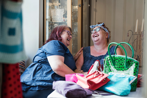 Two owners of a vintage clothing store looking at bags they are selling together sitting at a table in the North East of England.