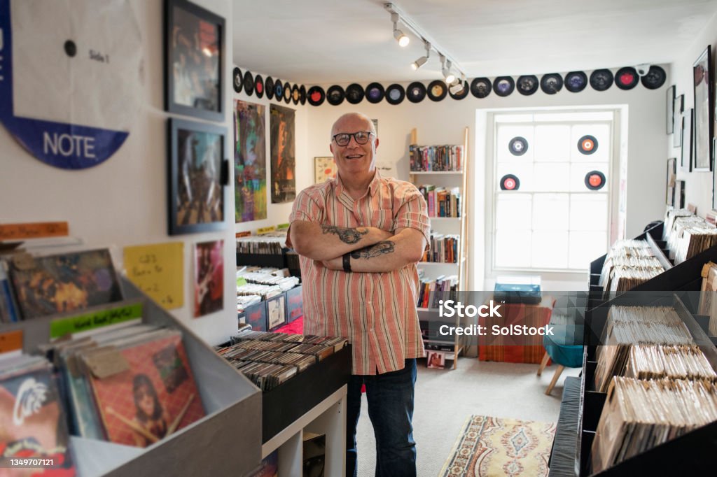 Proud of his Record Store Front view of the owner of a record store standing in his shop looking at the camera smiling with his arms crossed in the North East of England. Eccentric Stock Photo