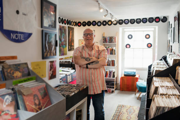Proud of his Record Store Front view of the owner of a record store standing in his shop looking at the camera smiling with his arms crossed in the North East of England. offbeat stock pictures, royalty-free photos & images