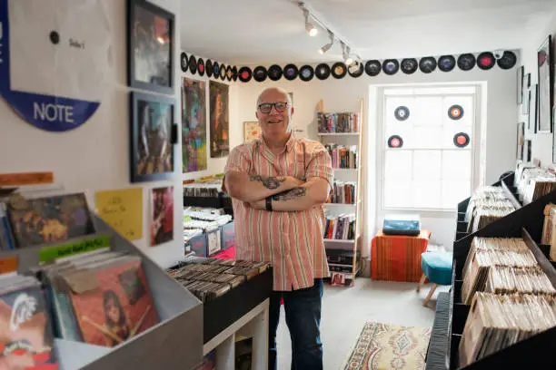 Front view of the owner of a record store standing in his shop looking at the camera smiling with his arms crossed in the North East of England.