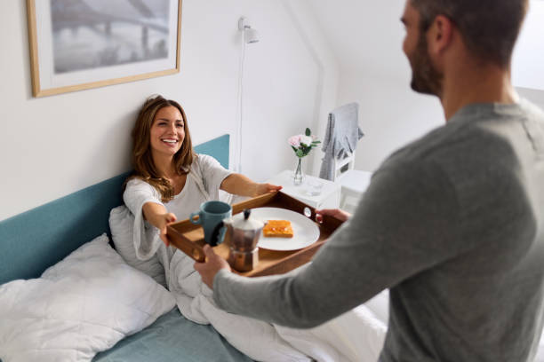 Loving man serving breakfast to beautiful woman in bed at home stock photo