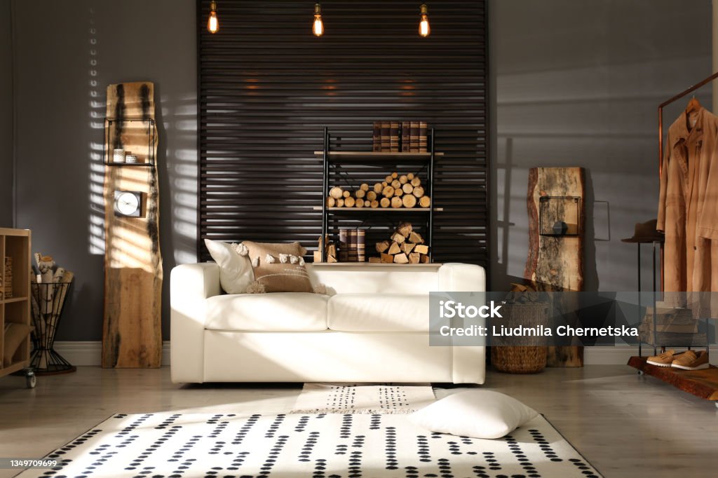 Shelving unit with stacked firewood and comfortable sofa in stylish room interior Rustic Stock Photo