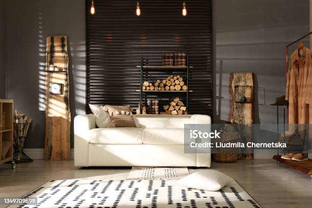 Shelving Unit With Stacked Firewood And Comfortable Sofa In Stylish Room Interior Stock Photo - Download Image Now