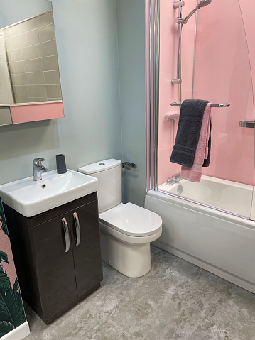 Stock photo showing close-up view of modern bathroom with grey and pink colour scheme, white, ceramic bathtub with glass shower panel and chrome towel rail with grey and pink towels.