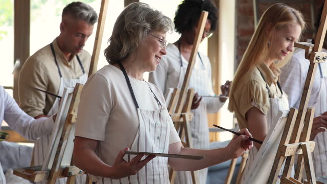 Diverse people painting with paintbrushes on easels in art studio