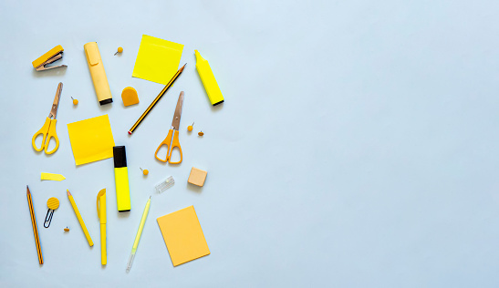 Top view of yellow stationery on blue background with copy space. Flat lay office supplies for back to school and creativity. Brainstorming session with blank sticky notes, scissors and pencils.