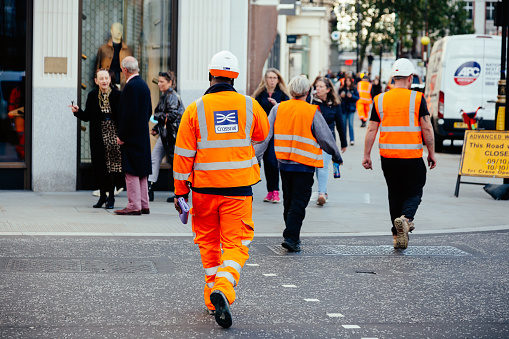 London, UK - 27 October, 2021: Crossrail railway workers in hardhats and protective workwear cross the street in central London, UK.