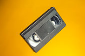 Copy of Old Analog Videocassette Tape VHS as Retro Nostalgia or Vintage Type of Media Format Over Yellow Background. Horizontal Image Composition