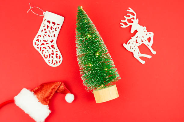 istock flat layout. top view. on a red background, a toy tree with lights, a santa hat, a white deer and a Christmas sock. 1349718678