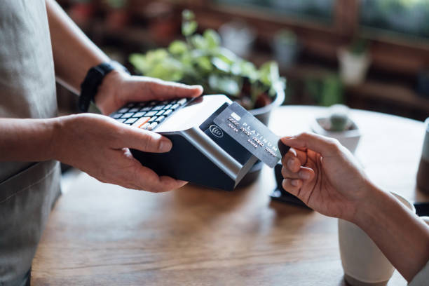 primo piano della mano di una donna che paga il conto con carta di credito in un bar, scansionando su una macchina per carte. pagamento elettronico. banche e tecnologia - consumerism foto e immagini stock