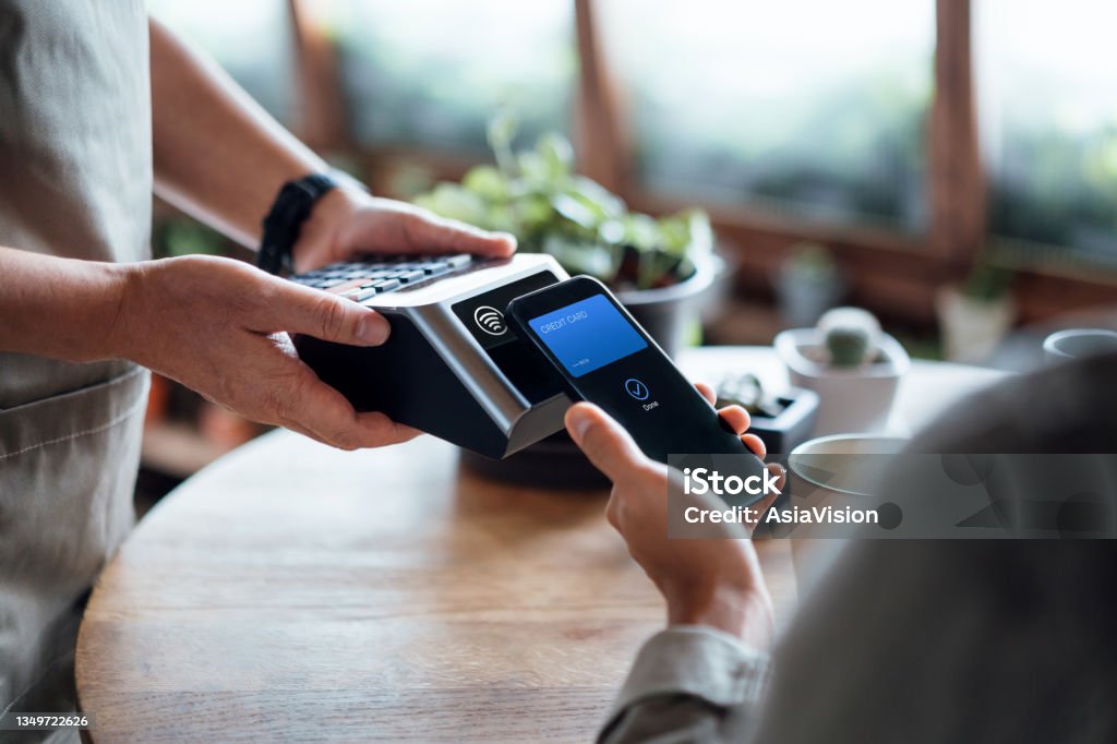 Close up of a male's hand paying bill with credit card contactless payment on smartphone in a cafe, scanning on a card machine. Electronic payment. Banking and technology Paying Stock Photo