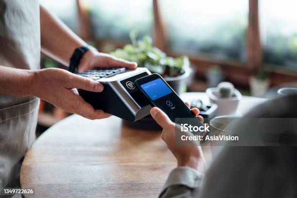 Close Up Of A Males Hand Paying Bill With Credit Card Contactless Payment On Smartphone In A Cafe Scanning On A Card Machine Electronic Payment Banking And Technology Stock Photo - Download Image Now