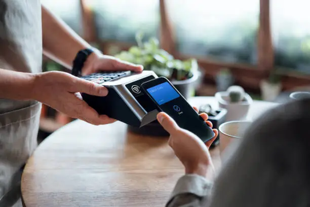 Photo of Close up of a male's hand paying bill with credit card contactless payment on smartphone in a cafe, scanning on a card machine. Electronic payment. Banking and technology