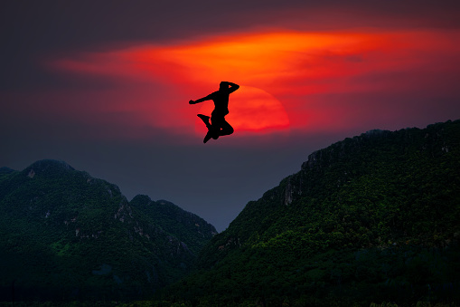 Silhouette of man jumping over mountain On the background of the evening sun