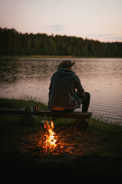 istock Man admiring lake sunset. Bonfire on a shore 1349729255