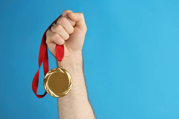 istock Man holding golden medal on blue background, closeup. Space for design 1349731999