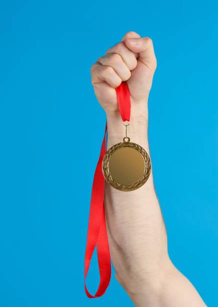 istock Man holding golden medal on blue background, closeup. Space for design 1349733115