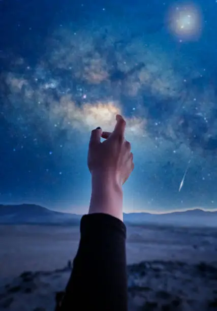 Photo of hand view, hand pointing or touching the starry sky with Milky Way and stars