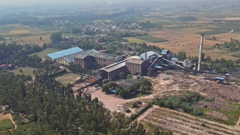 Aerial view of sugar mill factory in India surrounded by wheat crop fields and trees.
