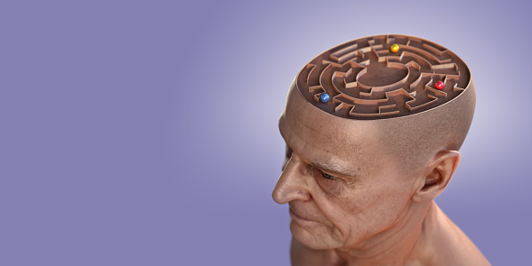 A digitally generated image of the head of a senior male viewed from above, with top section removed to reveal a maze containing three shiny red, blue and yellow balls. With a pastel purple background with subtle highlight behind the head. With selective focus on the front of the head.