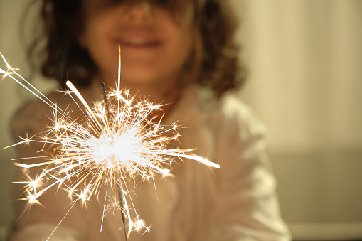 Caucasian girl smiling out of focus background with sparkler in hand in foreground