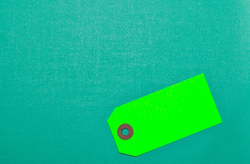Green blank label tag on a teal cardstock background with copy space, conceptual image.