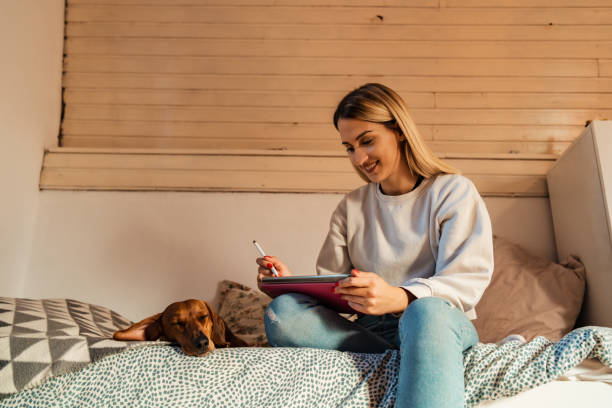 istock Modern woman, an graphic designer working on tablet from her bed while her dog lying near her 1349767497