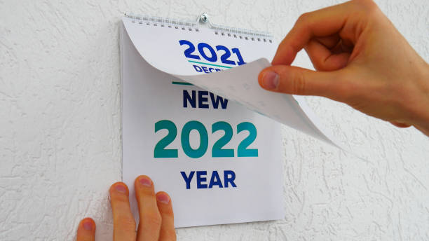 nahaufnahme von männlichen händen, die durch die dezemberseite des wandkalenders 2021 blättern, gefolgt von der titelseite eines neuen kalenders 2022 - kalender abreißen stock-fotos und bilder