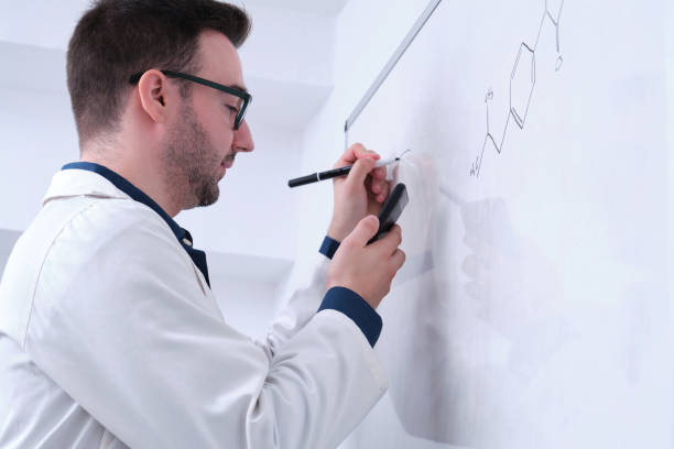 istock Male researcher in lab coat writing notes on whiteboard. 1349769536