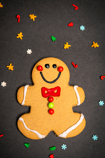 An overhead view of a gingerbread man cookie on black with sprinkles all around.