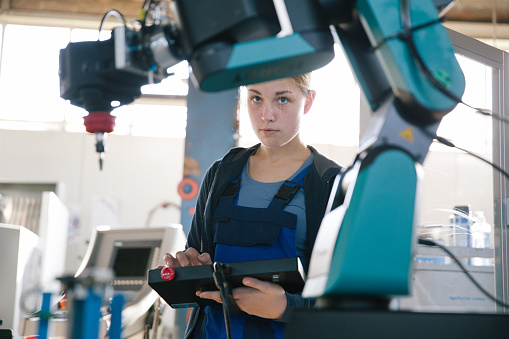 female student works on a robotic arm with an digital tablet