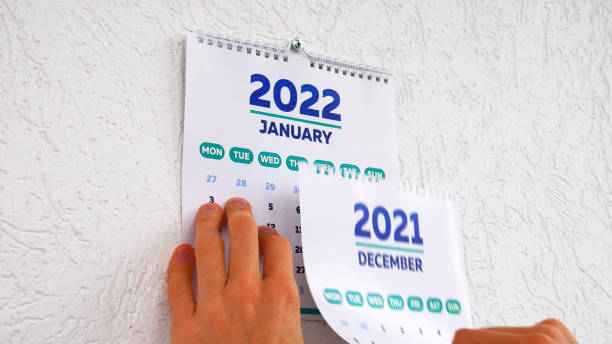 die hände eines mannes reißen die dezemberseite eines kalenders 2021 an der wand ab, gefolgt von der januar-seite eines neuen kalenders 2022 - kalender abreißen stock-fotos und bilder