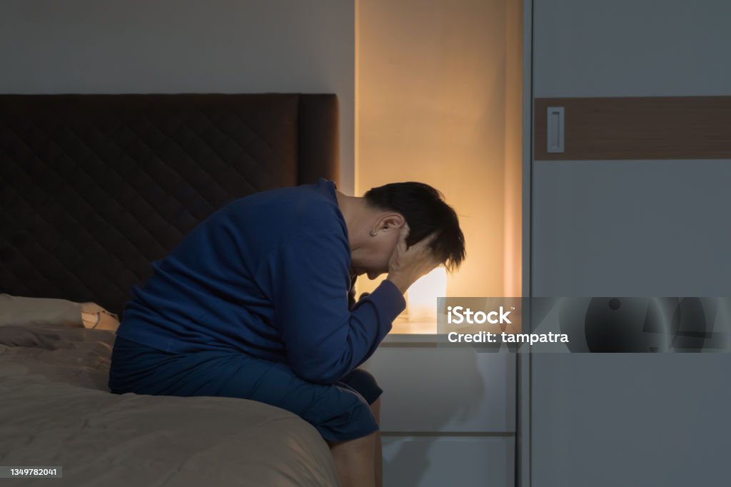 Depressed lonely elderly old Asian woman, people sitting on bed in bedroom at home. Lifestyle on late night. Insomnia. Quarantine Insomnia Stock Photo