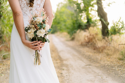 Girl dressed as a bride with a bouquet of preserved flowers between her hands on an out of focus background in nature. bouquet of dried flowers. Horizontal photograph