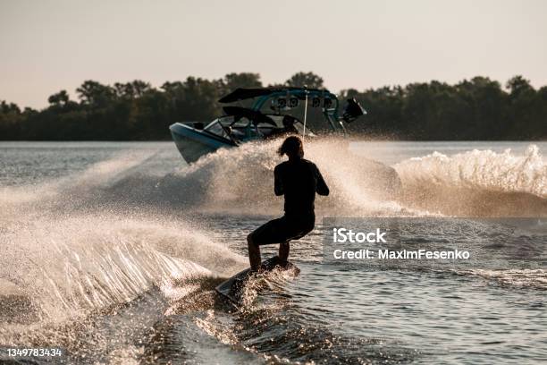 Rear View Of Active Man Riding Wakeboard Behind Motor Boat On Splashing River Waves Active And Extreme Sports Stock Photo - Download Image Now