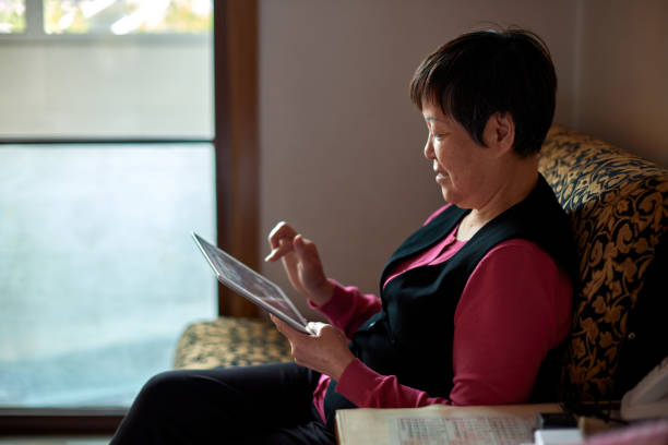 istock An old Asian woman uses a tablet computer on the sofa at home 1349783456