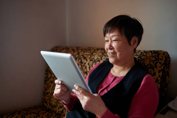 istock An old Asian woman uses a tablet computer on the sofa at home 1349783577