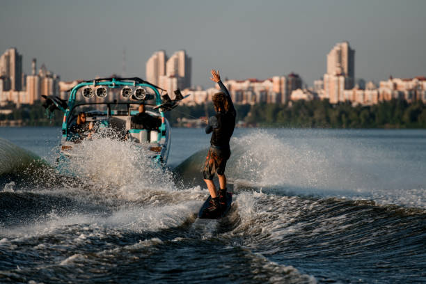 istock wakeboarder moving fast behind boat holding rope and riding on splashing river wave. 1349785624