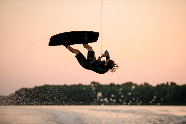 istock male wakeboarder skilfully jumping and flips on wakeboard over splashing wave 1349785747