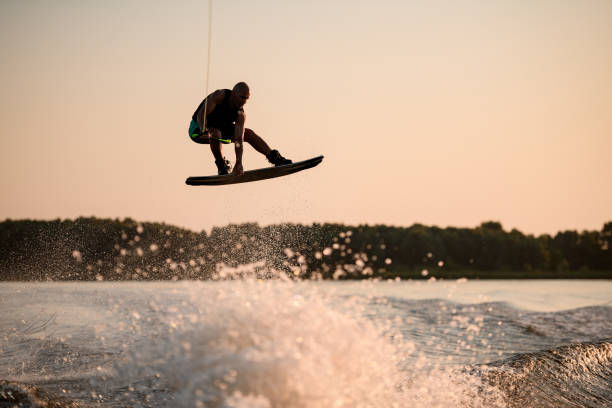 空を背景に水をはねかける上にウェイクボードで高く跳ね上がる筋肉の男 - wakeboarding waterskiing water ski sunset ストックフォトと画像