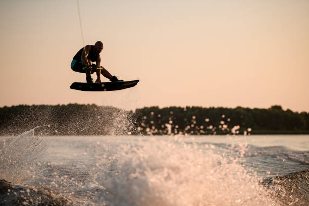 istock active muscular man jumping high with wakeboard over splashing water against the backdrop of sky 1349788000