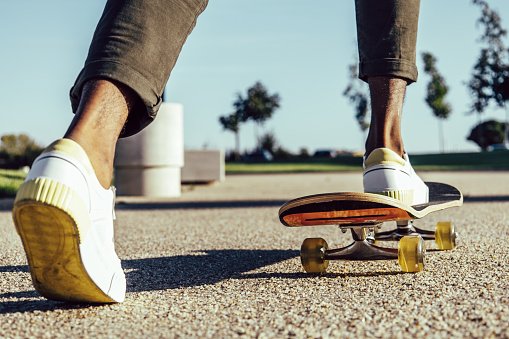 Closeup of black legs riding skateboard in park